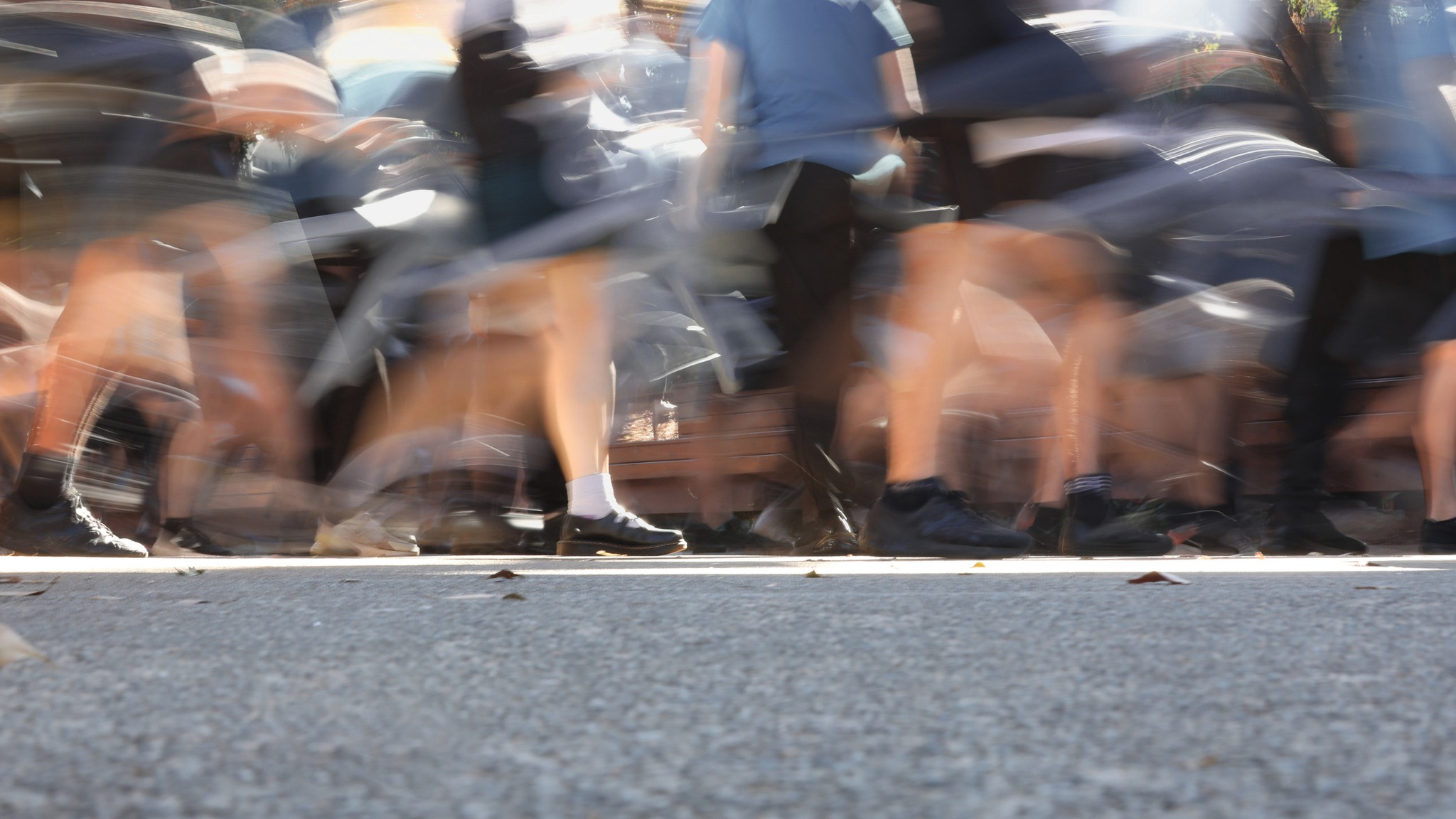 A deliberately blurred action or motion shot of school students (could be busy street also) walking outside between or to classes. Low angle showing legs moving and feet. Logos and brands removed or changed